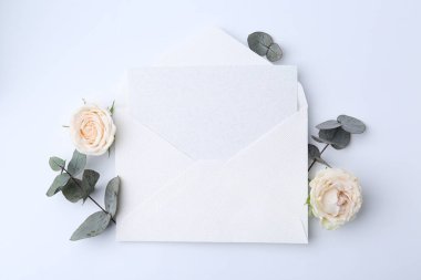 Zarfta boş tebrik kartı, okaliptüs yaprakları ve beyaz arka planda güller, üst manzara