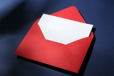 Koyu mavi arkaplanda kırmızı zarflı boş tebrik kartı, yakın plan.