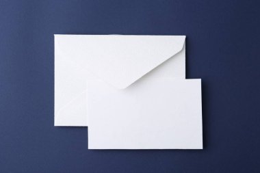 Koyu mavi zemin üzerinde boş tebrik kartı ve kağıt zarf, üst görünüm