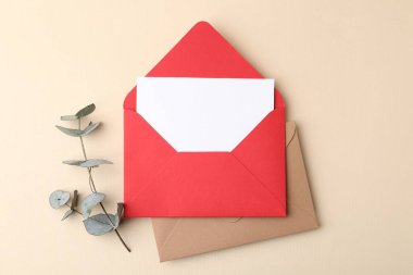 Boş tebrik kartı, zarflar ve okaliptüs yaprakları bej arka planda, düz uzanmış