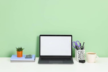 Modern dizüstü bilgisayarlı şık bir iş yeri açık yeşil duvarın yanındaki beyaz masada.
