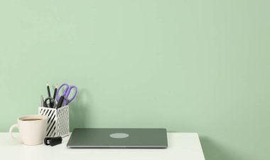 Modern dizüstü bilgisayarı açık yeşil duvarın yanındaki beyaz masada olan şık bir iş yeri. Metin için boşluk