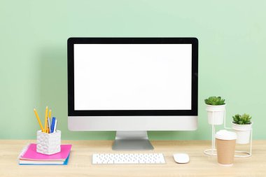 Modern bilgisayarlı şık bir iş yeri açık yeşil duvarın yanındaki ahşap masada.