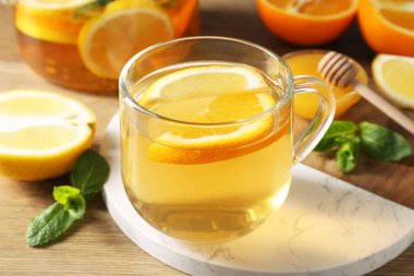 Cam fincanda aromatik meyve çayı, portakal, limon, bal ve nane, ahşap masada, yakın plan.