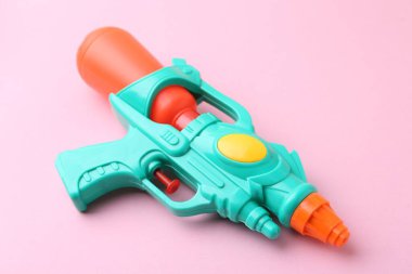 Açık pembe arka planda parlak plastik su tabancası, yakın plan.