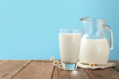 Taze süt ve çiçekler ahşap masada açık mavi arka planda, yakın plan. Metin için boşluk