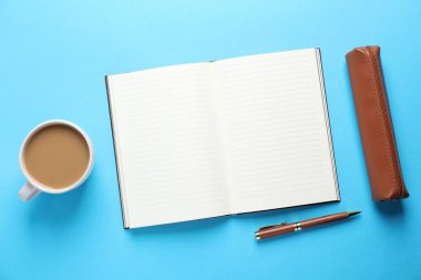 Boş defter, kalem kutusu, açık mavi zemin üzerinde kalem ve kahve, düz uzanma