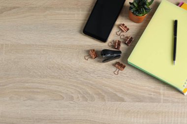Ofis malzemeleri, akıllı telefon ve ev bitkisiyle ahşap masa üzerinde düz bir kompozisyon. Metin için boşluk