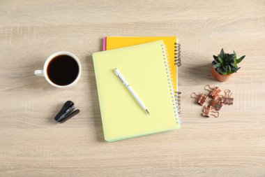 Ofis malzemeleri, bir fincan kahve ve ahşap masa üzerine konmuş ev bitkisi.