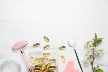 Beyaz mermer masa üzerinde kolajen kapsülleri ve çiçekleri ile düz bileşim yatıyordu