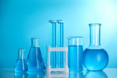 Aynanın yüzeyinde mavi arkaplana karşı sıvı bulunan laboratuvar camları.