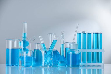 Aynanın yüzeyinde gri arka planda mavi sıvı bulunan laboratuvar camları