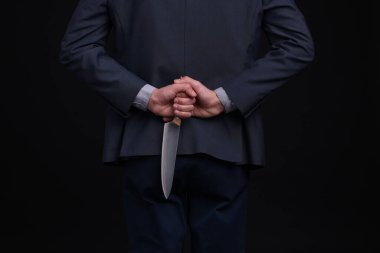 Siyah arka planda sırtında bıçak tutan bir iş adamı, yakın plan.