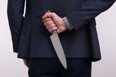 Beyaz arka planda sırtında bıçak tutan iş adamı, yakın plan.