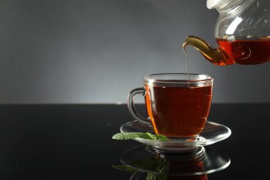 Koyu ayna masasında çaydanlıktan fincana taze demlenmiş çay doldurmak, yakın plan. Metin için boşluk