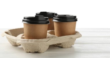 Kağıt kahve bardakları beyaz ahşap masadaki karton tutacakta, yakın plan.