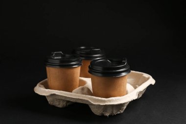 Siyah arka planda karton tutacakta kağıt kahve fincanları.