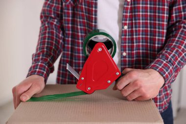Karton kutuyu kapalı bir yere kapatmak için yapıştırıcılı bant kullanan bir adam.