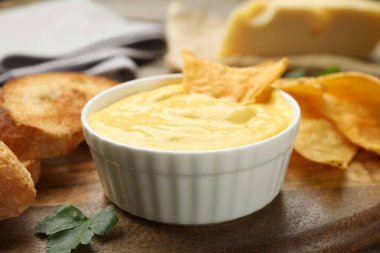 Lezzetli peynir sosu kasede, cips ve kızarmış ekmek masada, yakın plan.