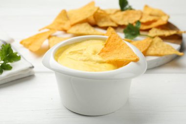 Lezzetli bir peynir sosu ve beyaz ahşap masada nacho cipsi, yakın plan.