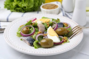 Ringa balıklı lezzetli salata, yumurta, hardal ve sebzeler beyaz fayanslı masada, yakın plan.