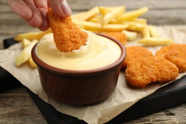 Ahşap masada tavuk parçalarını peynir sosuna batıran kadın, yakın plan.