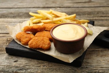 Tabakta nefis peynir sosu, tavuk nugget ve ahşap masada patates kızartması, yakın plan.