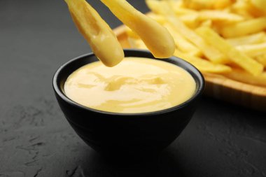 Siyah masada patates kızartmasını peynir sosuna batırmak, yakın plan.
