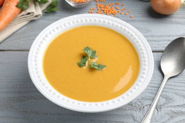 Gri ahşap masada servis edilen lezzetli mercimek kremalı çorba, yakın plan.