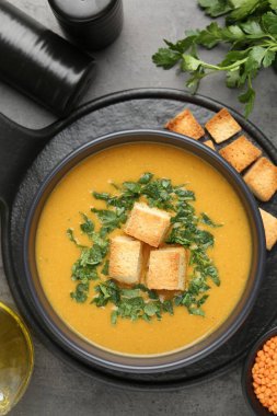 Lezzetli mercimek kremalı çorba. Gri masadaki kızarmış ekmeklerle servis ediliyor.