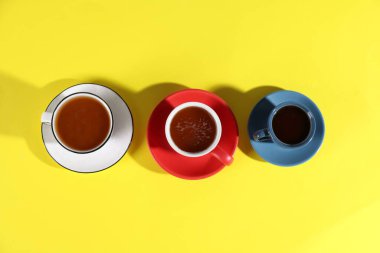 Sarı arka planda aromatik kahve içilen farklı bardaklar.