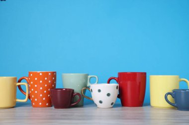 Açık ahşap masada mavi arka planda bir sürü renkli fincan var. Metin için boşluk