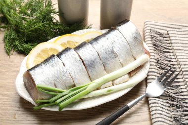 Limon dilimli lezzetli ringa balıkları, yeşil soğan ve ahşap masada dereotu, yakın plan.