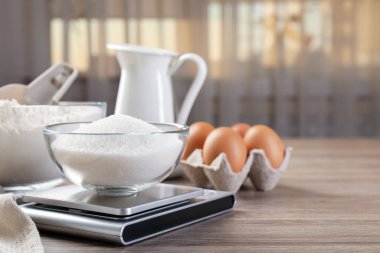 Dijital mutfak terazisi, bir kase şeker ve ahşap masa üzerindeki diğer ürünler, yakın plan. Metin için boşluk