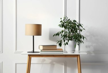 Çiçek, kitap ve lamba beyaz duvarın yanında.