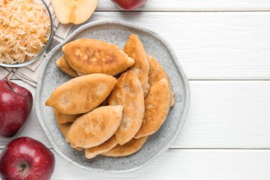 Lezzetli kızarmış pirizky (doldurulmuş turtalar) ve beyaz ahşap masa üzerinde elmalar, düz yatak. Metin için boşluk