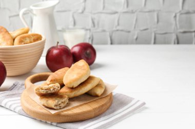 Lezzetli kızarmış pirizky (doldurulmuş turtalar) ve beyaz ahşap masada elmalar, yakın plan. Metin için boşluk