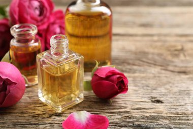 Ahşap masanın üzerinde aromatik esanslı yağlar ve güller olan parfüm şişelerini aç, yakın plan. Metin için boşluk