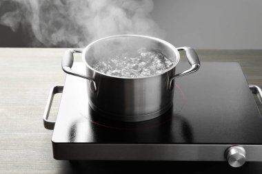 Kaynar suyla pişirme tenceresi ve ahşap masa üzerinde gri arka plan, yakın çekim