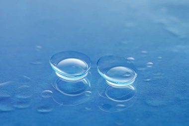 Mavi ayna yüzeyine bir çift kontakt lens ve su damlası, yakın plan.