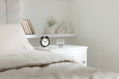 Komodinin yanında çalar saat ve yatağın yanında bir bardak su var.