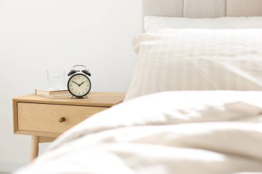 Alarmlı komodinli komodin, bir bardak su ve yatağın yanında kitap.