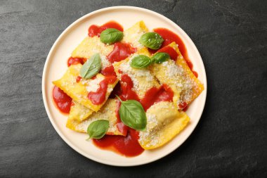 Domates soslu lezzetli ravioli, siyah masada parmesan peyniri ve fesleğen.