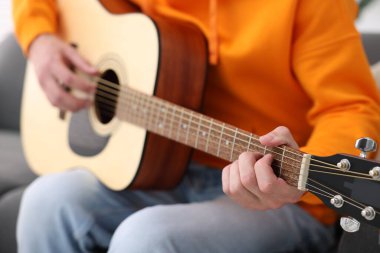 Genç adam kanepede gitar çalıyor, yakın plan.