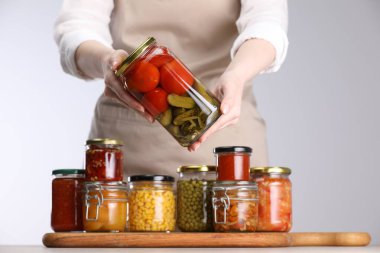 Açık gri arka planda farklı turşulu ürünlerle dolu kavanozları olan kadın, yakın plan.