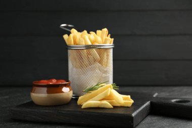 Lezzetli patates kızartması, ketçap ve biberiye ile servis ediliyor, siyah masada, yakın plan.