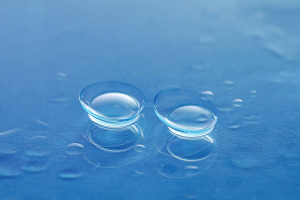 Пара контактных линз и капель воды на поверхности голубого зеркала, крупный план