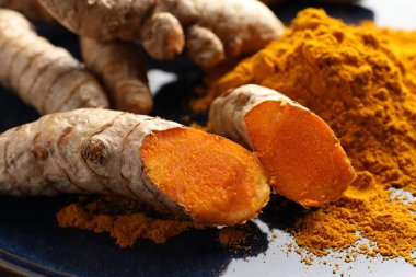 Aromatik zerdeçal tozu ve mavi tabakta taze kökler, yakın plan.