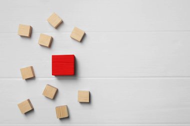 Farklı, eşsiz, özel. Beyaz masanın üstünde, düz yatanlar arasında kırmızı küp. Metin için boşluk