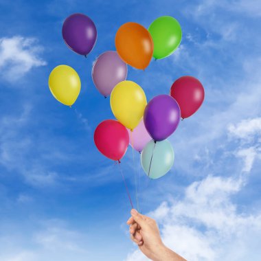 Adam elinden bir avuç balonu gökyüzüne salmak üzere, yakın plan. Özgürlük kavramı